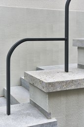 Eingangstreppe mit Natursteinstufen, vertikal gekämmtem Putz und schwarzem Stahlhandlauf