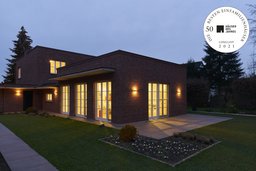 Gestaffelter Klinkerbau mit beleuchteter Terrasse und Garten in der Abenddämmerung