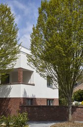 Gebäudeecke mit Backsteinmauer, integrierter Eckloggia und vorgelagertem Baumbestand