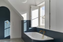 Badezimmer im Dachgeschoss mit Rundbogentür, blauer Wandvertäfelung und Messingarmaturen