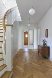 Zentrale Diele mit Eichen-Fischgrätparkett, geschwungener Holztreppe und Blick zum Eingang