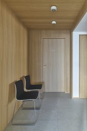 Holzvertäfelte Flurnische mit bündiger Praxistür, Deckenstrahlern und zwei Warteplätzen