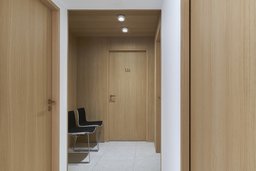 Blickachse durch den Praxisflur auf holzverkleidete Wartebereich mit Behandlungszimmertür