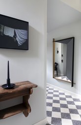 Eingangsbereich mit diagonal verlegtem Schachbrettboden, geometrischem Wandspiegel und Holzkonsole