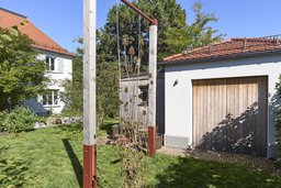 Gartenansicht mit Holzschaukel, Schuppen, Garage mit Holztor und Wohnhaus im Hintergrund