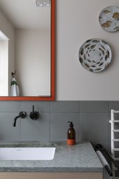 Badezimmer-Waschtisch aus Naturstein mit mattschwarzer Wandarmatur und rotem Spiegelrahmen