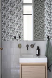 Gäste-WC mit floraler Mustertapete, hellgrauem Fliesenspiegel und minimalistischem Holzwaschtisch