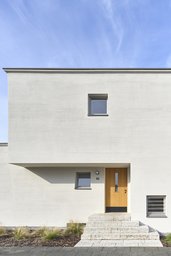 Überkragender Eingangsbereich mit Eichentür, massiven Natursteinstufen und feiner Putzfassade