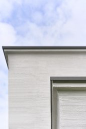 Fassadendetail mit horizontalem Besenstrichputz und profilierter Hohlkehle am Dachabschluss