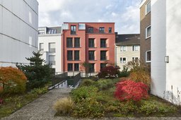 Fassade des rotverputzten Mehrfamilienhauses mit hellgrauem Klinkersockel, gerundeten Fensterlaibungen, seitlichem Vorsprung mit Tonnendach