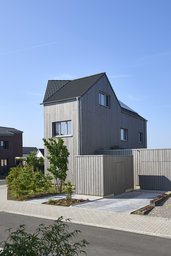 Straßenseitige Ansicht mit Stellplätzen, kubischem Nebengebäude und vertikaler Holzschalung