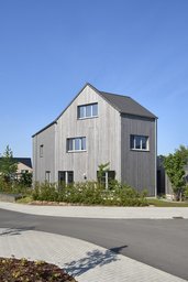 Straßenansicht über Eck mit vertikaler Holzfassade, Satteldach und Hecke