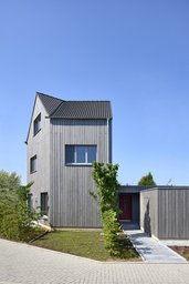 Straßenansicht mit gepflastertem Zugangsweg, roter Haustür und vertikaler Holzfassade