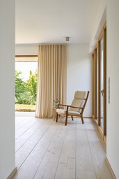 Lichtdurchflutetes Esszimmer mit Holzdielen, Sessel und bodentiefen Fenstern zum Garten