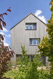 Gartenseitige Giebelfassade mit vertikaler Holzschalung hinter dichter Bepflanzung