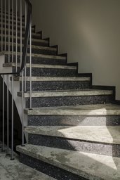 Gewendelte Steintreppe im Treppenhaus mit filigranem Metallgeländer