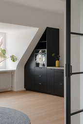 Maßgefertigte schwarze Einbauküche unter der Dachschräge neben hellem Gaubenfenster
