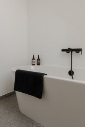 Freistehende weiße Badewanne mit mattschwarzer Wandarmatur vor gefliester Wand