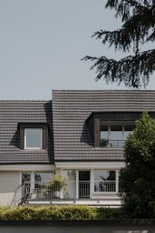 Ziegelgedecktes Steildach mit dunkel verkleideten Gauben und darunterliegendem Balkon