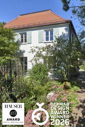 Gartenfassade mit rotem Walmdach, salbeifarbenen Fensterläden und blühendem Staudengarten
