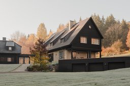 Gebäudeensemble am Hang mit Garagentrakt, Schleppgauben und dunkler Holzfassade