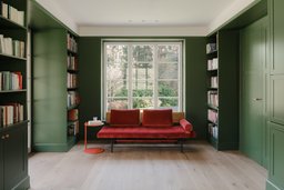 Dunkelgrüne Bibliothek mit maßgefertigten Einbauregalen, rotem Daybed und Sprossenfenster