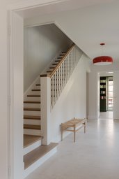 Helle Eingangsdiele mit klassischer Holztreppe, Natursteinboden und Blickachse zur Bibliothek