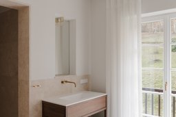 Elegantes Bad mit Holzwaschtisch, Messingarmatur, Natursteinwand und bodentiefem Sprossenfenster