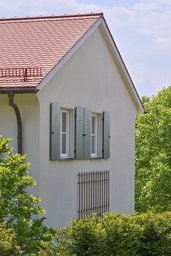 Giebelansicht mit rotem Ziegeldach, grünen Klappläden und filigranem Wandspalier