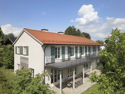 Zweigeschossige Gartenfassade mit rotem Satteldach, durchgehendem Balkon und überdachtem Freisitz