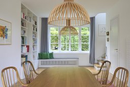 Essbereich mit Holz-Esstisch, Holzpendelleuchten, maßgefertigtem Bücherregal und integrierter Fenstersitzbank