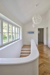 Helle obere Diele mit geschwungener Treppenbrüstung, horizontalem Fensterband und Fischgrätparkett