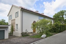 Straßenansicht des Einfamilienhauses mit heller Putzfassade, Klappläden und geschwungener Traufkante