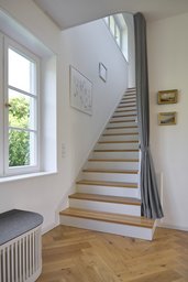 Geradlinige Holztreppe mit Eichen-Trittstufen, weißen Setzstufen und textilem Raumteiler-Vorhang