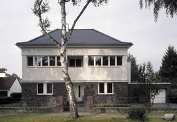 Frontalansicht der Straßenfassade mit Klinkersockel, weißem Obergeschoss und vorgelagerter Birke