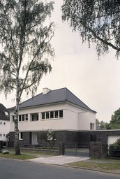 Perspektivische Straßenansicht mit Zufahrt, Garage, dunklem Klinkersockel und Walmdach