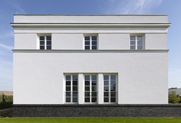 Symmetrische Fassadenansicht mit Klinkersockel, Gesimsbändern und dreiteiligen bodentiefen Sprossenfenstern