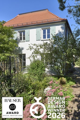 Gartenfassade mit rotem Walmdach, salbeifarbenen Fensterläden und blühendem Staudengarten